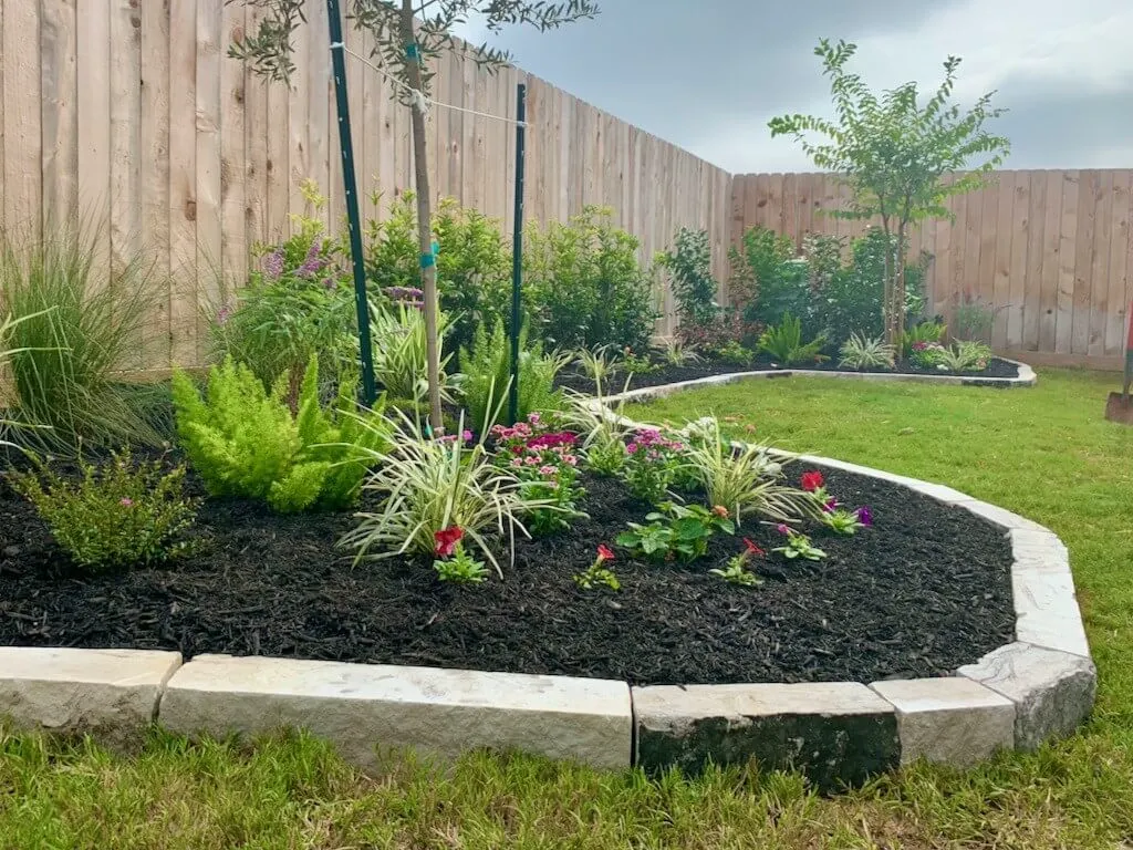 Front landscape bed finished with a natural stone border that separates planting areas from the lawn and gives the yard a sharper curb-appeal edge.